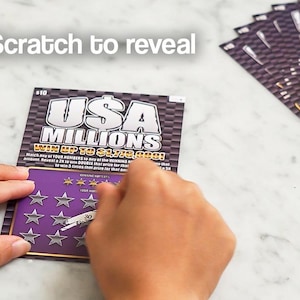 May include: A person scratching a "USA Millions" lottery ticket. The ticket has a purple background with silver stars and the text "Scratch to reveal". The text "WIN UP TO $1,779,000!" is also visible. Other tickets are in the background.