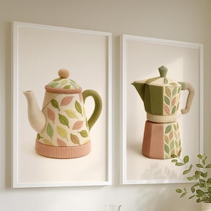 Puede incluir: Dos impresiones artísticas enmarcadas con diseños de punto con temática de té. Una impresión muestra una tetera beige con detalles de hojas verdes y amarillas. La otra impresión muestra una cafetera verde y beige con patrones de hojas.