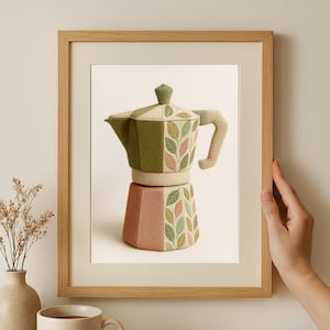 Op de afbeelding: Een ingelijste print van een koffiezetapparaat met een uniek ontwerp. Het koffiezetapparaat is voornamelijk groen, roze en beige, met bladerpatronen. De print zit in een lichtbruine houten lijst en een hand houdt de lijst vast.