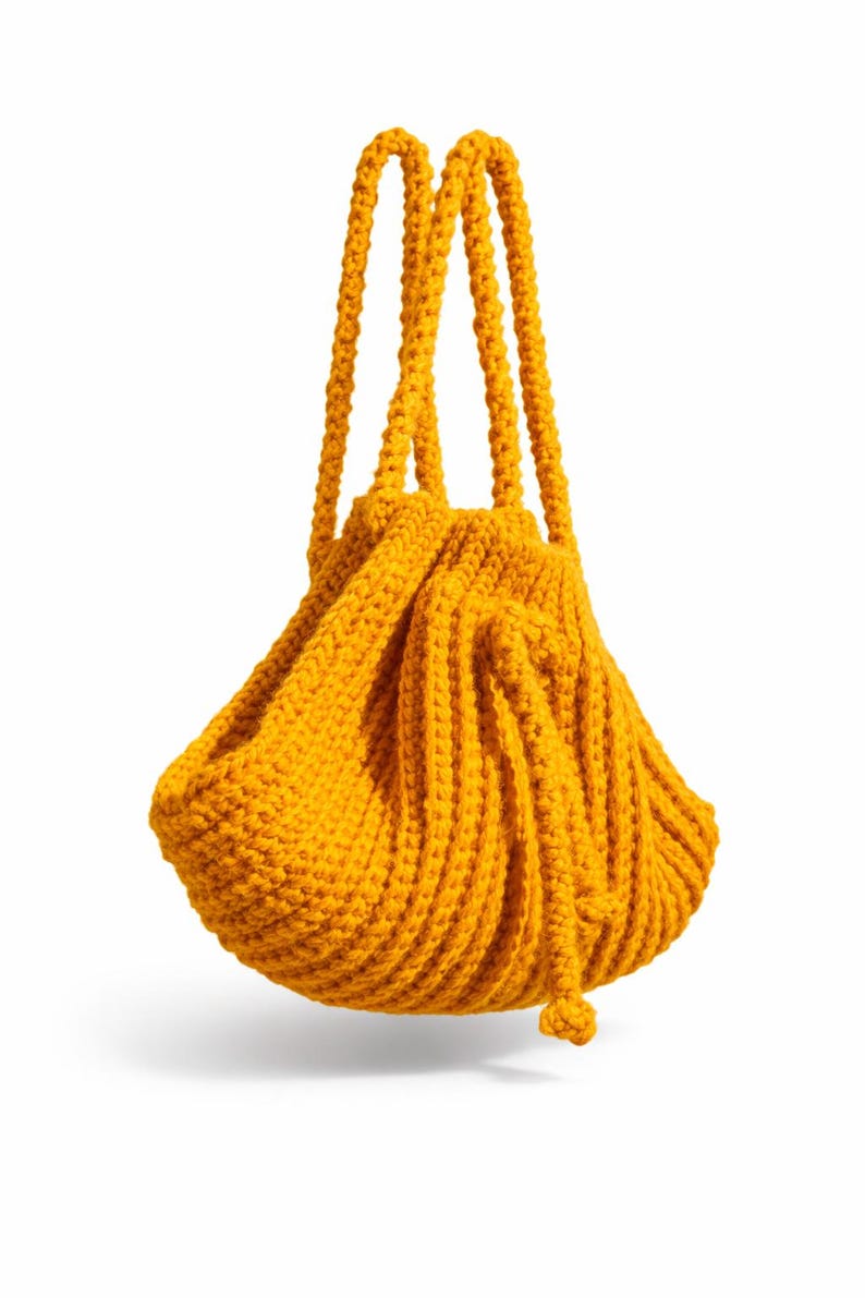 May include: A mustard yellow knitted drawstring bag with two thick, rope-like handles. The bag has a rounded, gathered shape and a textured, ribbed pattern. The drawstring closure is visible at the bottom.