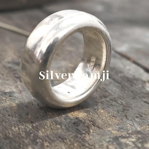 May include: A wide, polished silver ring with a rounded design. The ring has a smooth, reflective surface and appears to be made of solid metal. The text "Silver amji" is visible on the ring.