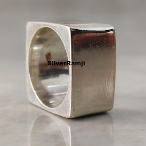 May include: A square silver ring with a hollow centre. The ring has a smooth, polished surface and a modern, minimalist design. The text "SilverRamji" is visible on the ring. This ring is a piece of jewellery.