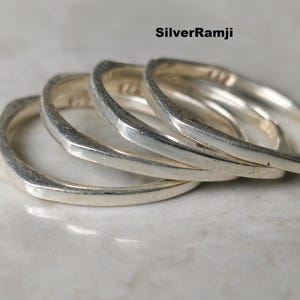 Könnte beinhalten: Vier silberne Ringe mit quadratischem Design sind übereinander gestapelt. Die Ringe bestehen aus glänzendem Metall und haben eine leicht strukturierte Oberfläche. Die Ringe werden auf einer hellen Oberfläche mit dem Text "SilverRamji" oben rechts angezeigt.