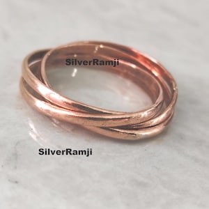 Peut inclure: Ensemble de trois anneaux en cuivre entrelacés, d'une teinte brun-rougeâtre chaude. Les anneaux sont imbriqués, créant un design unique. Le texte "SilverRamji" est visible sur les anneaux.