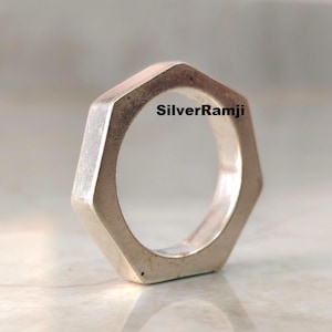 May include: A silver hexagonal ring with a solid, angular design. The ring has a polished finish and a geometric shape. The text "SilverRamji" is visible on the ring.