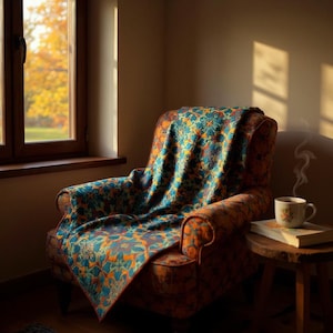Puede incluir: Un sillón tapizado con un estampado floral naranja está cubierto con una manta floral turquesa y naranja. Una taza de café está sobre una pequeña mesa de madera junto a un libro. La escena está iluminada por la luz del sol.