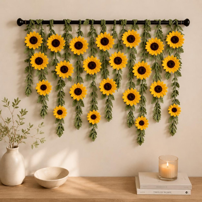 May include: A decorative wall hanging featuring yellow sunflowers with dark brown centers and green foliage. The sunflowers are arranged in a cascading pattern, suspended from a black rod. The wall hanging is a home decor item.