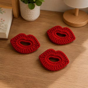 Peut inclure: Trois ornements individuels en crochet rouge en forme de lèvres. Chaque pièce est réalisée avec un point de fil texturé, formant une forme de bouche distincte avec un centre ouvert. La couleur rouge vive est uniforme sur les trois objets disposés en triangle.