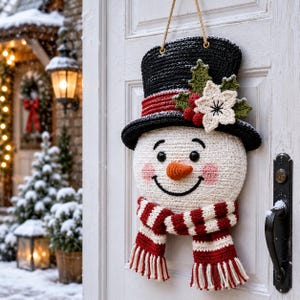 Peut inclure: Une d&eacute;coration de porte en crochet repr&eacute;sentant un bonhomme de neige avec un haut-de-forme noir &agrave; bande rouge, orn&eacute; de houx vert, de baies rouges et d'une fleur blanche. Il poss&egrave;de un visage blanc, des yeux noirs, un nez orange et une &eacute;charpe ray&eacute;e.