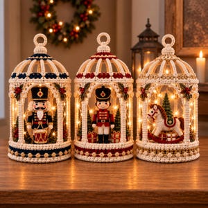 Pode incluir: Três ornamentos de crochê em forma de gaiola com luzes LED internas. A gaiola da esquerda contém um quebra-nozes com um tambor, a central um soldado e a da direita um cavalo de balanço. Cada gaiola é decorada com pequenas folhas verdes.