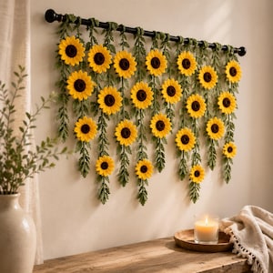 May include: A handcrafted wall hanging featuring yellow sunflowers with brown centers and green leaves. The sunflowers are attached to a black rod, creating a decorative floral display. The wall hanging is a charming piece of home decor.