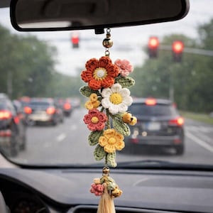 Peut inclure: Un charm de voiture fait à la main, en crochet, orné d'une cascade de fleurs colorées : orange, blanc, rose et jaune, avec des feuilles vertes. Le charme est suspendu au rétroviseur, ajoutant une touche florale à l'intérieur de la voiture.