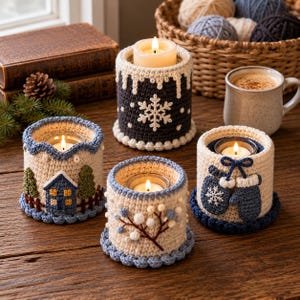 May include: Four cylindrical candle holders with crocheted covers featuring winter themes. One is dark gray with a white snowflake, one shows a house and trees, one has blue berries on a branch, and one features a pair of blue mittens with a bow.