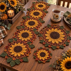Pode incluir: Um caminho de mesa, um lugar americano circular e um pequeno porta-copos de crochê, todos com um motivo de girassol com centros castanhos escuros, pétalas amarelas e folhas verdes. O conjunto é feito de fio e apresenta um design floral.