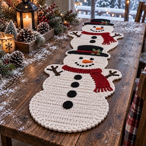 Pode incluir: Um caminho de mesa de crochê com um padrão repetitivo de três bonecos de neve. Cada boneco é branco com uma cartola preta, um cachecol vermelho, um nariz de cenoura laranja e botões circulares pretos alinhados verticalmente.