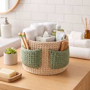May include: A beige and green crochet basket filled with white towels, tissues, and toiletries. The basket has two green pockets and holds toothbrushes and a comb. The basket is on a wooden surface.