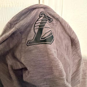 May include: A gray hooded sweatshirt with a black and white logo on the hood. The logo is a stylized letter "L" with a basketball design. The fabric has a heathered texture.