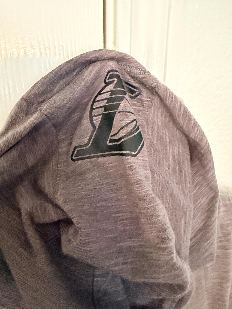 May include: A gray hooded sweatshirt with a black and white logo on the hood. The logo is a stylized letter "L" with a basketball design. The fabric has a heathered texture.