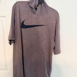 May include: A gray hooded shirt with short sleeves, featuring a black Nike swoosh logo on the front. The shirt has a textured appearance and a contrasting dark gray hood.