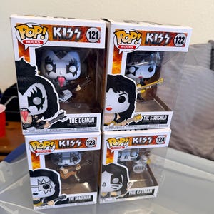 May include: Four Pop! Rocks KISS figures in their original boxes. The figures are of the band members: The Demon, The Starchild, The Spaceman, and The Catman. Each figure is in a clear plastic display case with the band's logo and figure number.