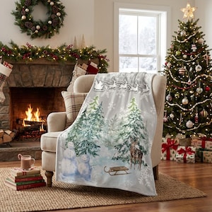 Può includere: Una coperta grigio chiaro con una scena invernale in stile acquerello raffigurante pini innevati, due pupazzi di neve, un cervo e una slitta di legno. Il bordo superiore mostra una sagoma bianca di Babbo Natale su una slitta con renne.