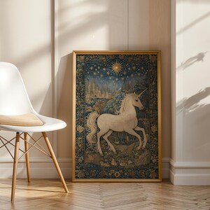 May include: A framed tapestry featuring a white unicorn with a long horn, set against a backdrop of a starry night sky and a medieval castle. The tapestry is in a gold frame and is displayed next to a white chair.