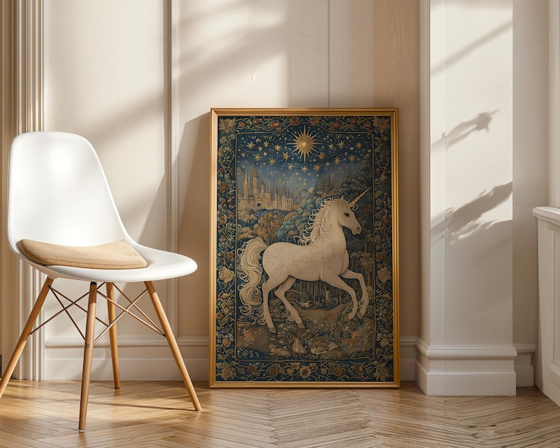 May include: A framed tapestry featuring a white unicorn with a long horn, set against a backdrop of a starry night sky and a medieval castle. The tapestry is in a gold frame and is displayed next to a white chair.