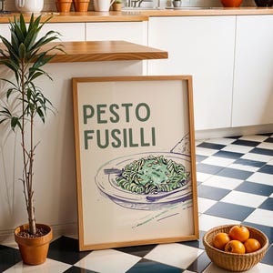 May include: A framed poster with the words "PESTO FUSILLI" in green lettering. The poster features an illustration of pasta with pesto on a plate. A small potted plant and a basket of oranges are next to the poster.