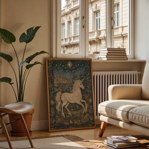 May include: A framed tapestry featuring a white unicorn in a forest scene, with a starry sky background. The artwork is displayed in a living room setting, alongside a potted plant, a wooden chair, and a beige sofa. The room has a window with a view of a building.