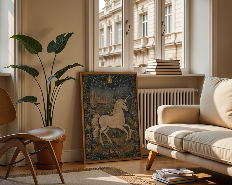 May include: A framed tapestry featuring a white unicorn in a forest scene, with a starry sky background. The artwork is displayed in a living room setting, alongside a potted plant, a wooden chair, and a beige sofa. The room has a window with a view of a building.