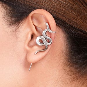 以下が含まれることがあります： 耳に巻き付く蛇の形をしたシルバーカラーのイヤーカフ。 蛇のデザインは、詳細な鱗と湾曲した体を持っています。 まっすぐなシルバーのバーが耳たぶから伸びています。 ジュエリー。