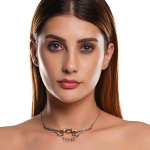 K&ouml;nnte beinhalten: Eine silberfarbene Halskette mit einem dekorativen Design mit roten und gelben Akzenten. Die Halskette hat eine zarte Kette und kleine, h&auml;ngende Elemente, die ein elegantes und detailliertes Schmuckst&uuml;ck schaffen.