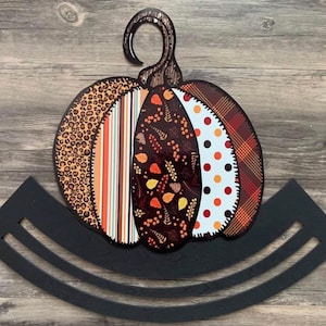 May include: A black metal pumpkin-shaped wreath hanger with a colorful pumpkin design featuring a variety of patterns, including leopard print, stripes, and floral designs.