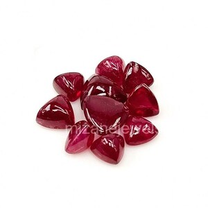 May include: A cluster of triangular, deep red gemstones. The polished stones are grouped against a white background. The gems have a glossy finish and varying shades of red. The Mizane Jewels logo is in the bottom right corner.
