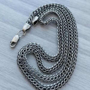 May include: A silver-toned chain necklace featuring a dense, woven foxtail or wheat link pattern. The necklace is constructed with multiple interconnected metal strands and is secured with a polished lobster claw clasp at the end of the chain.