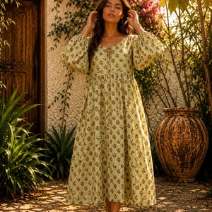 May include: A midi-length dress in a pale yellow hue featuring a vertical pinstripe pattern and a repeating small floral print. The garment has long, voluminous puff sleeves with gathered cuffs, a round neckline with a central tie, and a skirt.