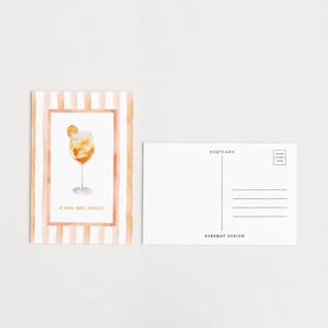 Könnte beinhalten: Eine Postkarte mit einer Aquarellillustration eines Cocktails in einem Weinglas, garniert mit einer Orangenscheibe. Die Postkarte hat einen gestreiften Pfirsich- und Weißrand und den Text "A small make cheers". Die Rückseite ist leer mit Linien zum Schreiben.