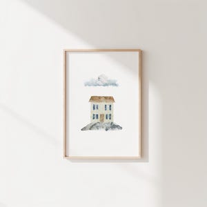 Puede incluir: Pintura a la acuarela de una casa de dos pisos con techo marrón, ventanas azules y puerta azul, sobre una base rocosa. Una nube esponjosa flota sobre la casa. La obra de arte está enmarcada en un marco de madera clara.