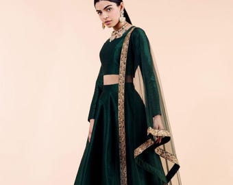 May include: A dark emerald green formal dress with long sleeves and a full skirt. The dress features gold trim along the neckline and a matching sheer scarf. The outfit is a traditional style, suitable for special occasions.