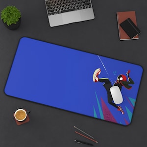 May include: A blue rectangular mousepad featuring a graphic of a superhero in a dynamic pose. The superhero is wearing a black suit with red accents and a mask. The mousepad has a black border and a white mouse is on the pad.