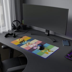 May include: A rectangular mousepad with a colorful design featuring cartoon characters. The pad has a striped background in yellow, pink, blue, and green. A black and blue mouse sits on the pad, next to a computer monitor.