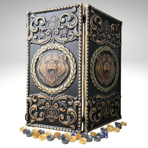 Puede incluir: Un juego de backgammon negro y dorado con un diseño tallado detallado. El juego presenta un oso rugiente en una corona de laurel en la parte delantera. Incluye fichas y dados. Un juego decorativo y funcional.
