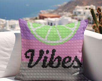 May include: A decorative pillow with a cross-stitch design. The pillow features a lime slice graphic in green and white, with the word "Vibes" in black. The background colors are pink, purple, and gray.