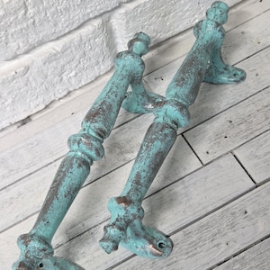 May include: Two antique-style door handles with a distressed turquoise finish and bronze accents. The handles are made of metal and have a decorative design, perfect for adding a vintage touch to any door or cabinet.