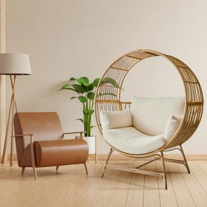 May include: A modern living room scene featuring a brown leather armchair and a unique, circular rattan chair with cream-colored cushions. A floor lamp and potted plant add to the room's decor. The room has light-colored walls and a wooden floor.