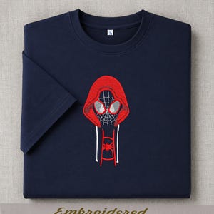 May include: Navy blue t-shirt with a red embroidered Spider-Man design. The design features a hooded Spider-Man with a spiderweb face and a spider emblem. The word "Embroidered" is printed at the bottom.