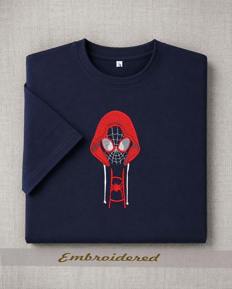 May include: Navy blue t-shirt with a red embroidered Spider-Man design. The design features a hooded Spider-Man with a spiderweb face and a spider emblem. The word "Embroidered" is printed at the bottom.