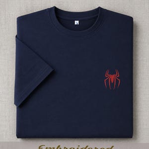 May include: Navy blue t-shirt with a red spider emblem embroidered on the chest. The shirt has short sleeves and a crew neck. The word "Embroidered" is printed in gold at the bottom of the image.