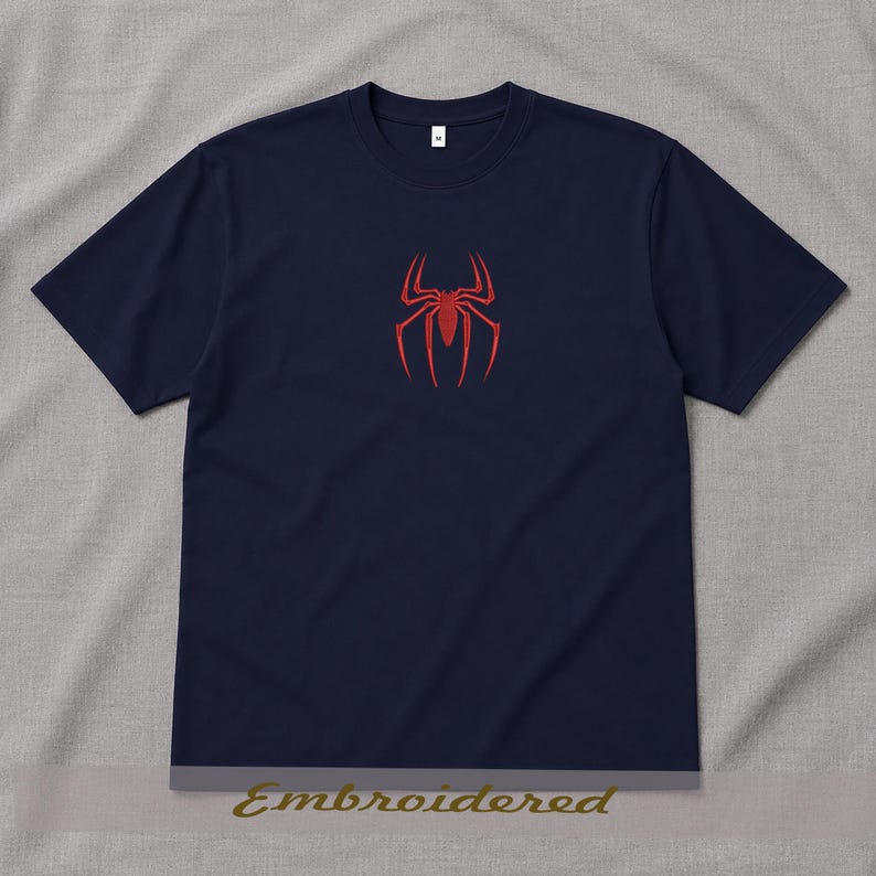 May include: Navy blue t-shirt featuring a red spider emblem on the chest. The shirt has short sleeves and a crew neck. The word "Embroidered" is printed at the bottom of the image. This tee is a casual wear item.