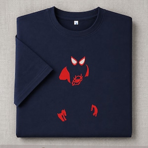 May include: Navy blue t-shirt with a red embroidered Spider-Man design. The design includes the character's eyes, spider emblem, and hands. The word "Embroidered" is printed at the bottom of the image.